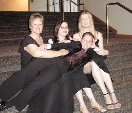 Picture of butch me lying across the laps of the other four writers (Kallmaker, Watts and Johnson). They're on carpeted stairs and we're all in formal wear (me in a tux).